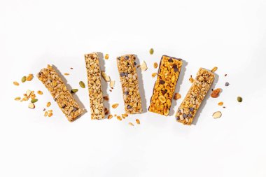 Beyaz bir yüzeyde çeşitli granola çubukları dağınık fındık ve tohumlar, sağlıklı atıştırmalıklar, genel görünüm