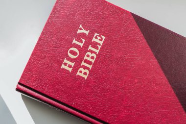 A close-up view of a red Holy Bible book with a textured cover and gold lettering during daylight clipart