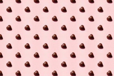 Heart-shaped chocolate pieces arranged on a soft pink background, Valentine's day backdrop clipart