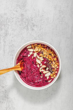 Granola ve bademle kaplı parlak ve kremalı meyve suyu kasesi.