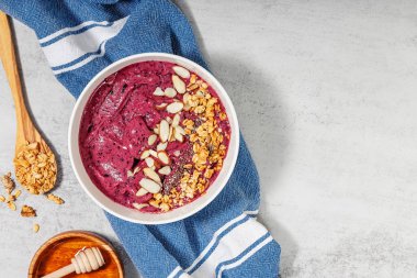 Mutfak havlusunda servis edilen granola ve bademlerle kaplı meyve suyu kasesi.