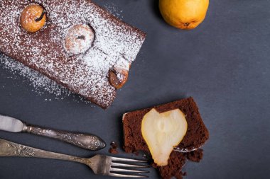 Koyu arka planda armut garnitürlü nefis nemli çikolatalı pasta eski tip çatal bıçaklarla servis edilir.