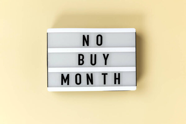 A sign displays the phrase No Buy Month against a soft, neutral background. Spending-free month, financial awareness and minimalism.