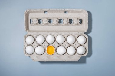 Mavi arka planda, beyaz yumurtalar arasında parlak sarı sarısı olan kartondaki yumurtalar.