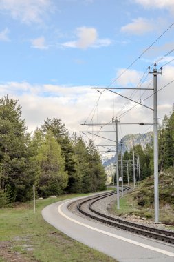 İsviçre 'deki dağların yakınlarındaki yemyeşil arazide kıvrılan manzaralı tren yolu.