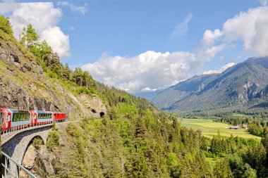Canlı kırmızı bir tren, İsviçre 'nin çarpıcı dağlık bir bölgesinde dolambaçlı bir yol boyunca ilerliyor.