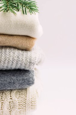 Açık arkaplanda yeşil bir çam dalı ile kaplı, nötr renklerde örülü bir kazak yığını.