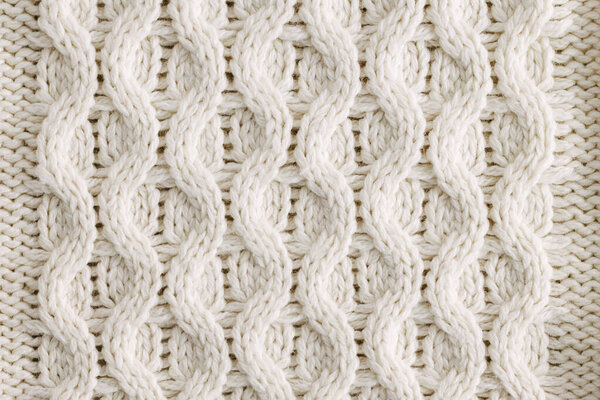 Крупный план узора из белой вязаной шерсти, с замысловатыми швами. Текстура подчеркивает мягкость и теплоту материала.