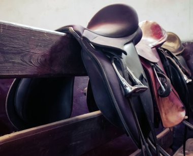 Tahta bir korkulukta duran at eyerleri. Sahne, binicilik ekipmanlarının binicilik faaliyetlerine hazırlanma ruhunu yakalıyor..