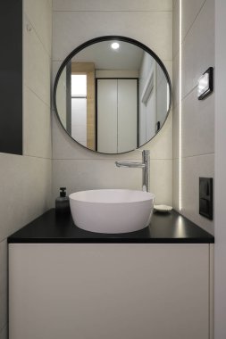 Seramik lavabolu musluk ve banyo içinde yuvarlak ayna.