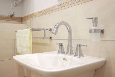 Banyo içinde beyaz seramik lavabo olan krom musluk.