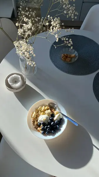 上图是装饰有家居装饰的白色餐桌 还有一碗带早餐水果的麦片 光影兼有 免版税图库图片