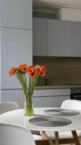 在木制和灰色丑闻的厨房前餐厅的白色圆桌 典雅的北欧风格 玻璃花瓶中的花朵和室内装饰 免版税图库图片