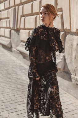 Şehir sokaklarında siyah dantelli maksi elbise giyen zarif bir kadının yaz portresi. Doğal güneş ışığı. Modelin arkasındaki şehir binaları.
