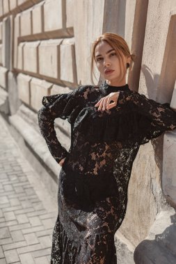 Şehir sokaklarında siyah dantelli maksi elbise giyen zarif bir kadının yaz portresi. Doğal güneş ışığı. Modelin arkasındaki şehir binaları.