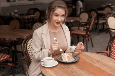 Genç ve zarif bir kadın çay ve turtayla kahvaltı yapıyor. Fransız kafesinin terasında oturuyor.