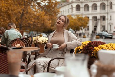 Genç ve zarif bir kadın sonbaharda Fransız Kafe 'sinin terasında çay ve turtayla kahvaltı yapıyor.