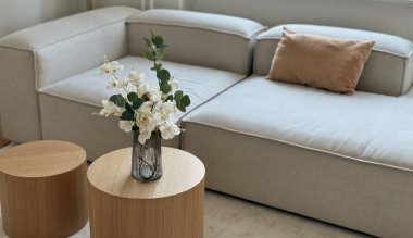 Kanepenin yanındaki yuvarlak ahşap bir masada vazoda suni çiçek buketi, sahte bitki odası dekorasyonu.