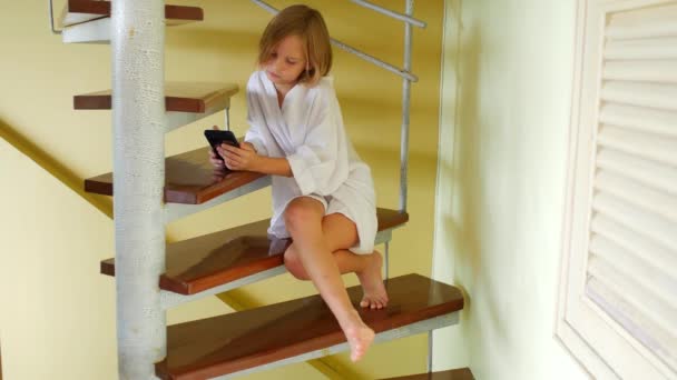 階段に座っている間 8歳の少女は 携帯電話のテープを介して反転 — ストック動画