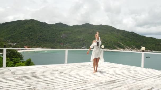白いドレスを着た美しい少女が踊り 海と島の景色を楽しむ — ストック動画