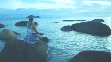 Denizde bir taşın üzerinde meditasyon yapan bir kadın..