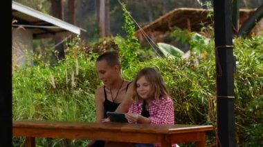 Anne ve kızı dinlenme alanındaki parkta dinleniyorlar. Aile telefonda oyun oynuyor..