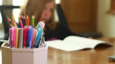 Liseli bir kız ödevini yapar. Çocuk bir deftere yazıyor. Yorgun çocuk, öğrenmek istemiyor, sıkılmış. Ön planda bir kutu kalem ve kalem var..
