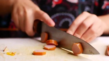 Çocuk bıçakla sandviç yapmak için sosis kesiyor.