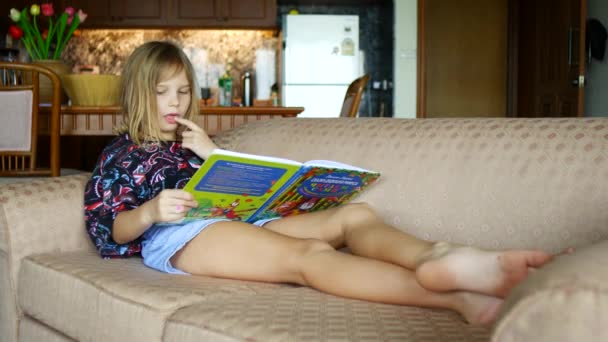 这个女孩正在沙发上看书 这孩子在学读书 — 图库视频影像