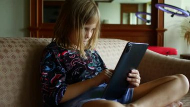 Kız okulda evden ders çalışıyor. Bir tablette çevrimiçi öğrenim