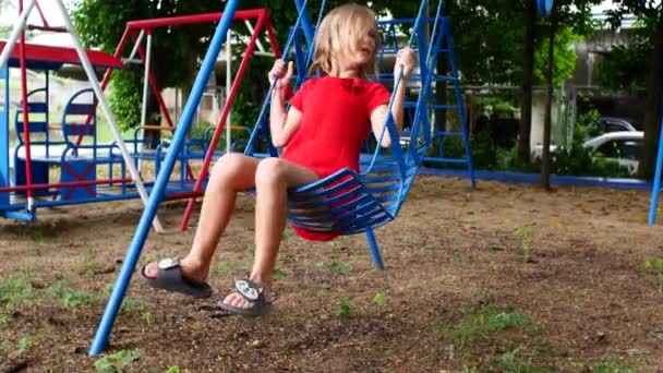 Egy Vörös Ruhás Kisgyerek Boldogan Himbálózik Város Játszóterén Zöld Van — Stock videók