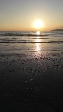 Denizin üzerinde gün batımının dingin güzelliğini hissedin, altın güneş ufkun altına batarken, sakin suların yavaşça kumlara değdiği sakin plajın üzerinde ılık bir turuncu parıltı salıyor.