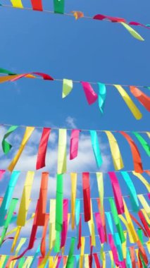 Açık hava kutlamalarının neşeli atmosferini hissedin canlı renkli kurdeleler açık mavi gökyüzünün arka planına karşı zarafetle sallanarak sokak dekoruna şenlik cazibesi ve heyecan katar.