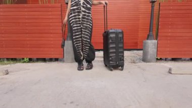 Şık bir kadın valiziyle bekliyor, seyahatin ruhunu büyüleyici ağır çekimde somutlaştırıyor, unutulmaz bir yolculuk için zemin hazırlıyor.