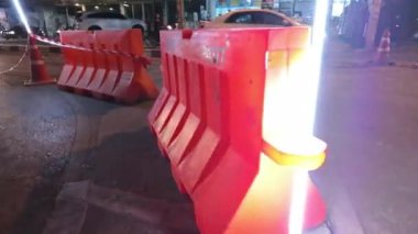 Bölge kırmızı bariyerlerle kordon altına alınırken ve gece bakımında güvenlik ve görünürlük sağlamak için sinyal lambalarıyla aydınlatılırken, gece yol onarımı sahnesi. İnşaat için ideal
