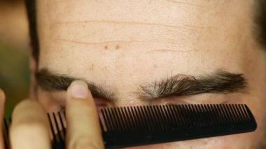 Profesyonel stilist bir adamın kaşlarını titizlikle tarar ve budardı, onları parlak bir görünüş için makasıyla şekillendirirdi. Bakım dersleri, erkek modası ve kişisel bakım içeriği için ideal