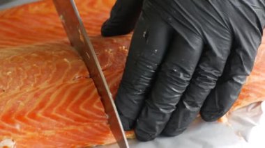Bir şefin eldivenli elleriyle füme somon filetosunu incelikle dilimlemesi, gurme mutfağındaki uzmanlık ve hassasiyeti gözler önüne seriyor..