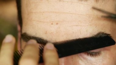 Profesyonel stilist bir adamın kaşlarını titizlikle tarar ve budardı, onları parlak bir görünüş için makasıyla şekillendirirdi. Bakım dersleri, erkek modası ve kişisel bakım içeriği için ideal