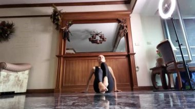 Siyah tulumlu, kel, orta yaşlı bir kadın evde dans ediyor.