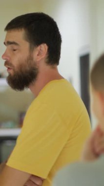 Sakallı ve yüzünde yoğun bir ifade olan bir adamın görüntüsü. Konuşma sırasında öfkesini dile getirirken ellerini kaldırıyor. Kapalı alanda sığ bir alanda çekilen, konuştuğu kişi bulanık.