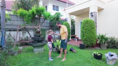 Erkek ve genç kız çimlerin üzerinde çıplak ayakla yürür, her biri güneşli bir arka bahçede birlikte hareket ederken ellerinde bir bitki tutarlar. Sıradan giyinip, bahçe eldivenleri giyip takım çalışmasını seviyorlar.