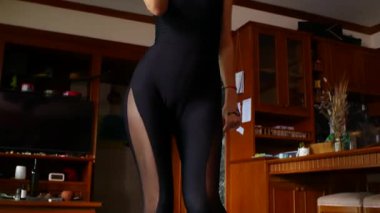 Siyah tulumlu, kel, orta yaşlı bir kadın evde dans ediyor.