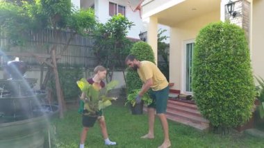Erkek ve genç kız çimlerin üzerinde çıplak ayakla yürür, her biri güneşli bir arka bahçede birlikte hareket ederken ellerinde bir bitki tutarlar. Sıradan giyinip, bahçe eldivenleri giyip takım çalışmasını seviyorlar.