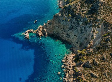 Berrak turkuvaz sularıyla çarpıcı bir kayalık kıyı şeridinin havadan görünüşü, kıyı bölgesinin doğal güzelliğini ve engebeli manzarasını gözler önüne seriyor.