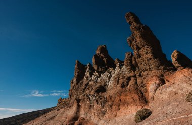 Sivri tepeleri ve dokulu yüzeyleri parlak mavi bir gökyüzünün altında dramatik kayalık oluşumlar.