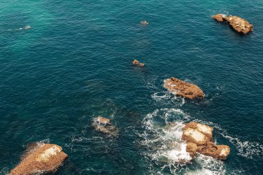 Dağınık kayalık oluşumları ve yumuşak dalgaları olan derin mavi okyanus manzarası