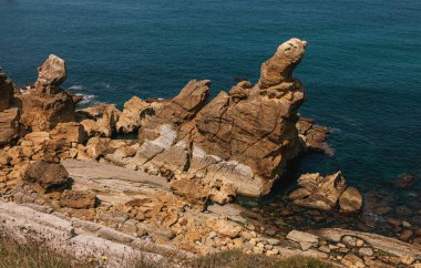 Unique rock formations along a rugged coastline with layered geological patterns meeting the deep blue ocean under a clear sk clipart