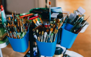 Mavi kaplarda renkli fırça çeşitleri, canlı ve yaratıcı bir çalışma alanı sunan araçlarla dolu.