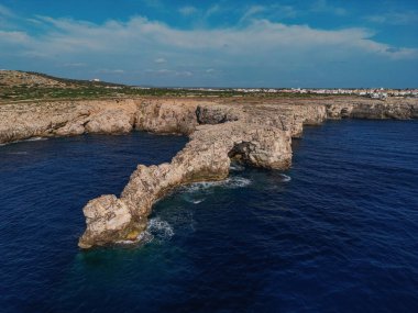 Doğal kaya kemeri engebeli kıyı şeridi ve berrak gökyüzüne uzanan derin mavi denize doğru uzanır.