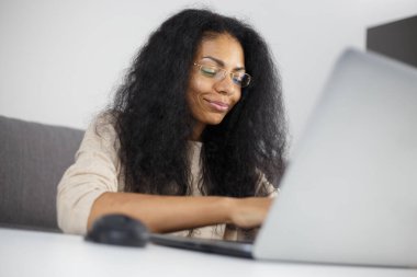 Cheerful black woman typing text on notebook keyboard at home. POC entrepreneur works on modern laptop computer with a smile